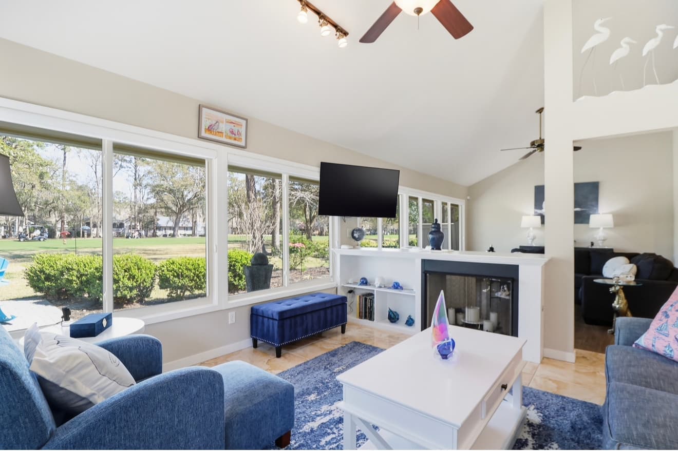 A vaulted living room with a white fireplace and windows onto a golf fairway