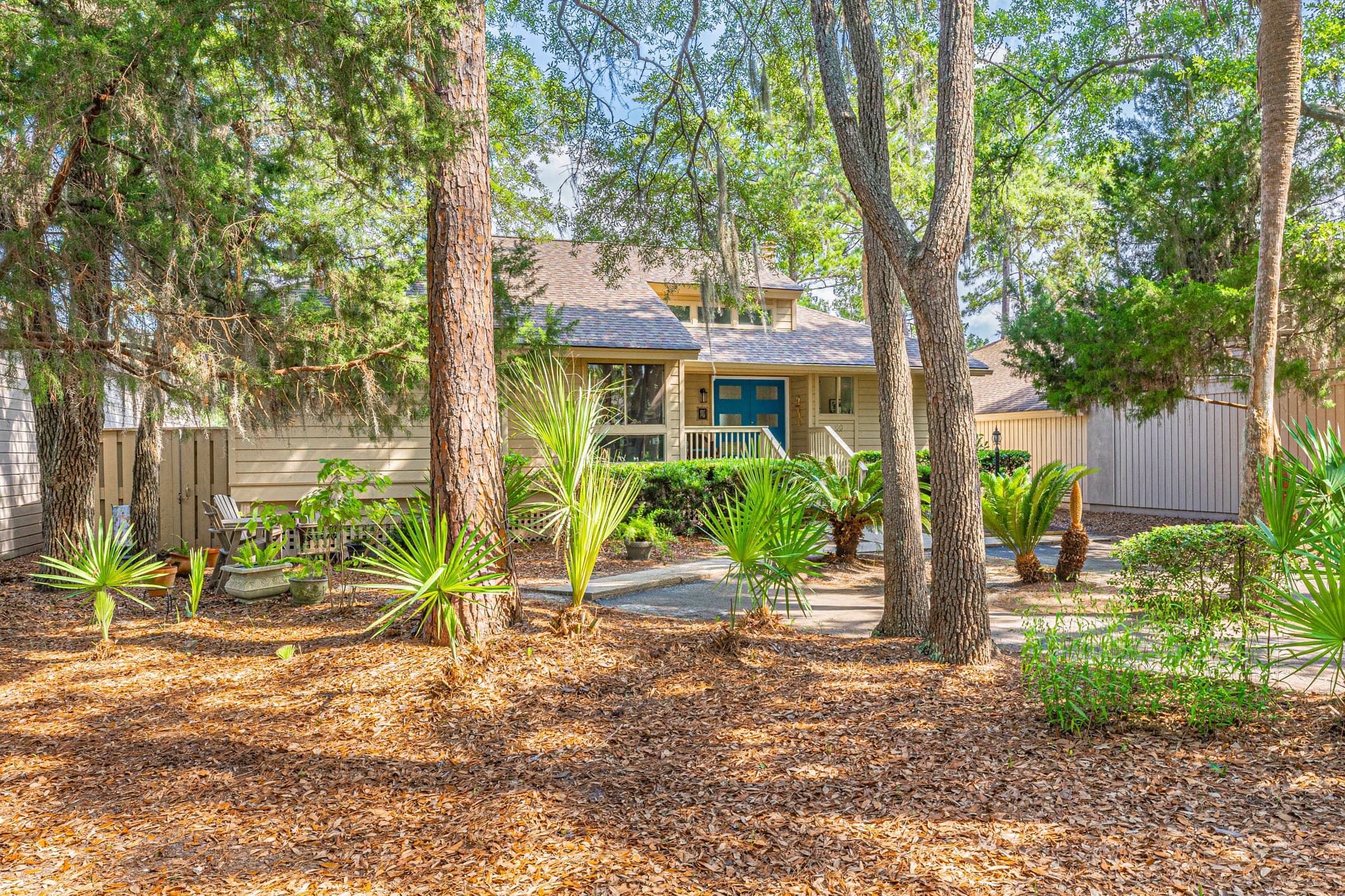 The front of 13 Marsh Winds in Moss Creek, Bluffton, under pines with a blue front door
